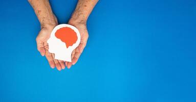 Top view of head with a brain made from paper on the palm senior woman over a blue background photo