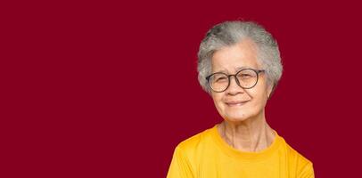 Portrait of an elderly Asian woman with short gray hair looking at the camera with a smile while standing on a red background photo