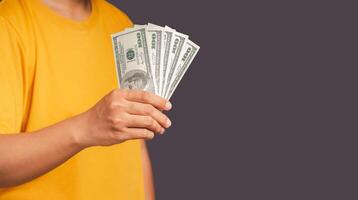 Man in an orange casual holding US banknotes while standing on gray background photo