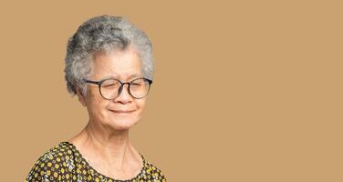 Portrait of a senior woman with short gray hair looking down with a smile while standing on a brown background photo
