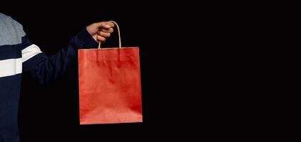 Hand holding a red paper bag with a handle on a black background photo