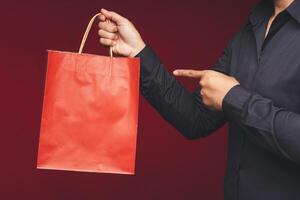 Close-up of hands holding and pointing to a red paper bag with a handle while standing on a red background photo