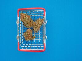 Top view of dried cannabis buds flower in a shopping cart on a blue background. photo