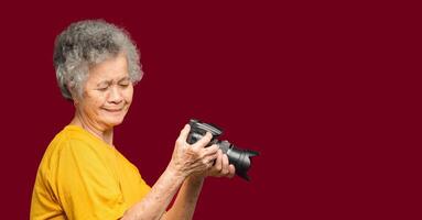 Happy senior woman looking at her photos in a digital camera while standing on a red background