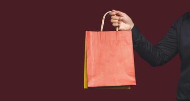 Close-up of hand holding a red paper bag with a handle while standing on a red background photo