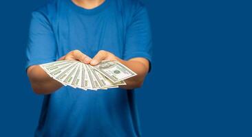 Man in a blue casual holding US dollar banknotes while standing on a blue background photo