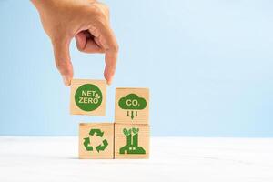 Net-zero CO2 emissions target in 2050. Hand holding of a wooden cube with green icons over a marble floor against a light green background photo