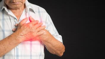 A senior man in a white shirt has sore left chest pain while standing on a black background photo