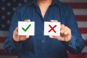 Close-up of hands holding two white papers with a green checkmark and red cross while standing on the American flag background photo