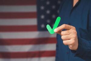 Hand holding a green check mark symbol while standing on the American flag background photo