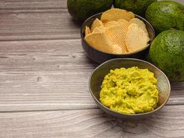 Top view of fresh guacamole in a dish and potato chips on a plate over a wooden table photo