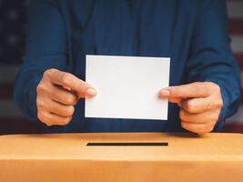 Hands voter holding ballot paper putting into the voting box at place election with an American flag background photo