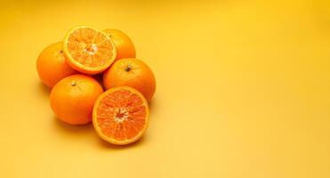 Pile of fresh oranges whole and half fruit on a yellow background with copy space for text photo