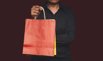 Close-up of hand holding a red and yellow paper bag with a handle while standing on a red background photo