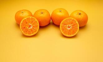 Pile of fresh oranges whole and half fruit on a yellow background with copy space for text photo