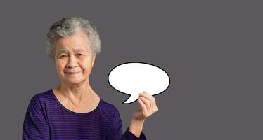Portrait of an elderly Asian woman is holding a blank speech bubble with a smile and looking at the camera while standing on a gray background photo