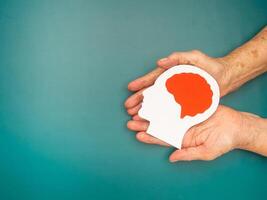 Top view of head with a brain made from paper on the palm senior woman over a green background photo