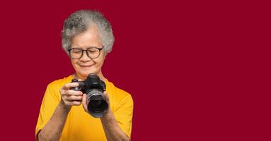 Happy senior woman looking at her photos in a digital camera while standing on a red background
