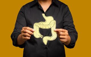 Close-up of hands holding a colon symbol while standing on a yellow background. photo