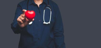 Close-up of hand doctor holding a red heart shape while standing on gray background photo
