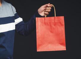 Hand holding a red paper bag with a handle on a black background photo
