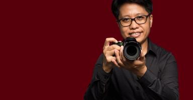 Portrait of a photographer in a black shirt holding a digital camera while standing on a red background photo