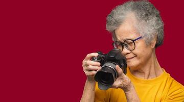 Senior woman taking photographs with a digital camera while standing on a red background photo