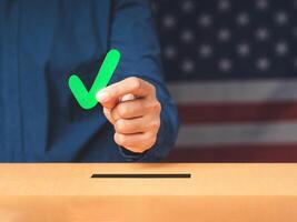 Hand holding a green check mark symbol overhead the voting box at place election with an American flag background photo