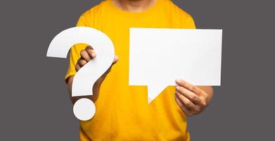 Close-up hand holding question mark symbol and a blank white speech bubble while standing on a gray background photo