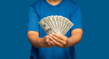 Man in a blue casual holding US banknotes while standing on a blue background. Business and finance concept photo