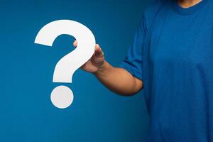 Close-up of hand holding a white question mark paper symbol while standing on a blue background photo