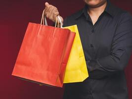 Close-up of hand holding a yellow and red paper bag with a handle while standing on a red background photo