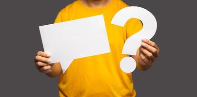 Close-up of hands young man holding a blank white speech bubble and a question mark symbol while standing on a gray background photo