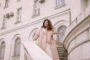 woman in elegant coat and hat against an intricate architectural backdrop, harmoniously blending modern fashion with historical allure. The soft daylight adds to its timeless appeal. photo