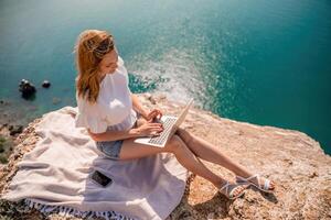 Freelance woman working on a laptop by the sea, typing away on the keyboard while enjoying the beautiful view, highlighting the idea of remote work. photo