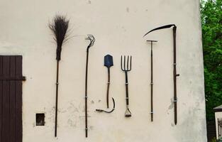 On the wall of the shed hangs a set of gardening tools. photo