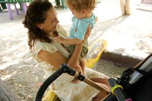 Mother joyfully lifting her toddler in a sunny park setting photo