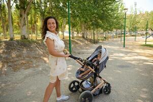 Mother smiling while walking with stroller in sunny park pathway photo