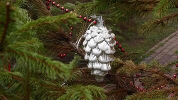 Bauble in shape of silver glittered pine cone hanging at fir tree branch swayed by wind. Rain instead of snowing in winter holiday due to climate change and global warming. Christmas tree outdoors video