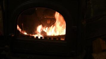 Rustic fireplace with burning firewoods and glowing flame inside with bright sparks in slow motion. Cozy warm light in furnace in night darkness. Natural fiery background with copy space video