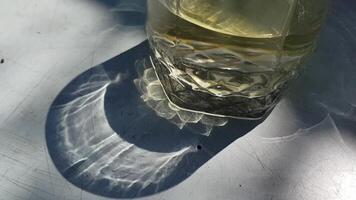 Shadow from whiskey glass in bright sunlight shining through ornate glass. Blurry wavy patterns of light and shadow on grunge table surface video