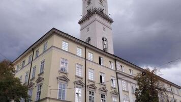 Tilt view to tower building exterior. Stormy clouds over ancient Town Hall in European city. Architecture in Viennese Classical style. Lviv town hall clock tower at Market Square. Camera moves up video