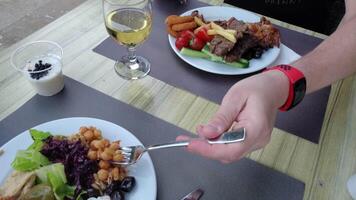 Time lapse of two people eating various food from dishes until plates become almost empty. Unrecognizable person eating lunch using knife and fork, drinking white wine from wineglass video