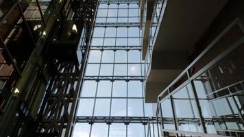 White clouds float outside the corporate building window glass wall. Modern elevator rise up and go down in time lapse. Reflections in mirrored wall of business skyscraper video