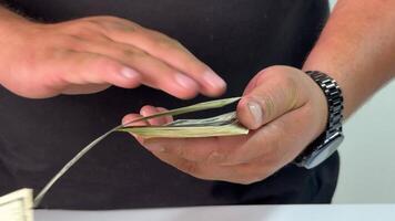 A hand gently slides a stack of cash across a table while counting bills. The setting offers a clear view of the intricate details of the currency being handled video