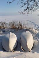 two boats on the shore of a lake in winter are standing under the snow photo