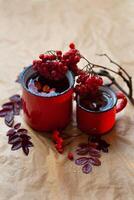 two red mugs with tea, a branch of autumn rowan lies nearby photo