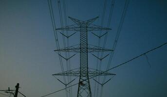 A towering electricity pylon with power lines stretches across the sky at dusk, creating a silhouette against the fading light, symbolizing energy and infrastructure. photo