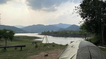 A tent is set up on the grass next to a river photo