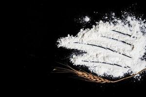 Wheat ears and flour on black background photo